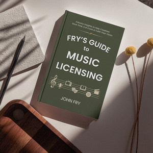 Book titled 'Fry's Guide to Music Licensing' by John Fry on a surface with a pen and dried flowers.