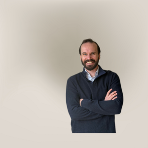 Man with a beard wearing a dark sweater on a beige background.